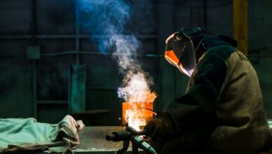 Welder working in an industrial workshop with sparks and smoke.