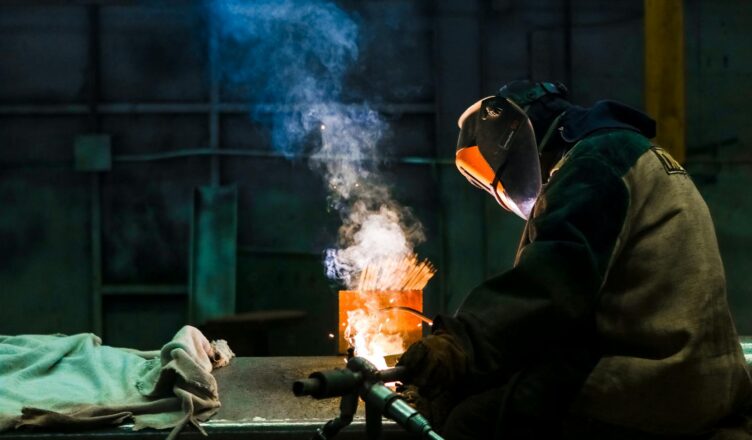 Welder working in an industrial workshop with sparks and smoke.
